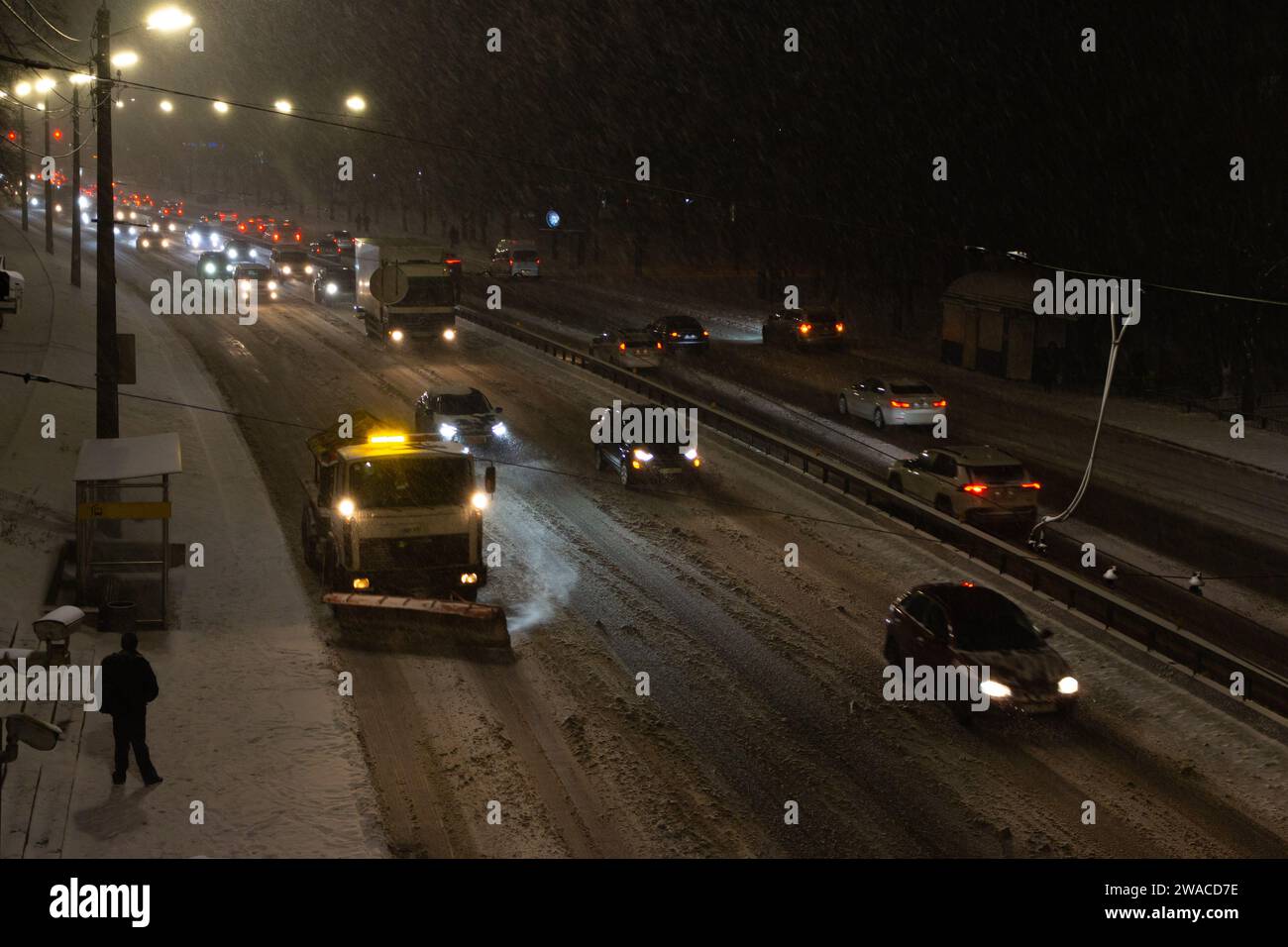 Schneefräse und Autos auf der Autobahn im Schneesturm. Winter in der Stadt. Winter-Servicefahrzeug bei der Arbeit bei Nacht. Kaltes, schneebedecktes Wetter in der Stadt. Stockfoto