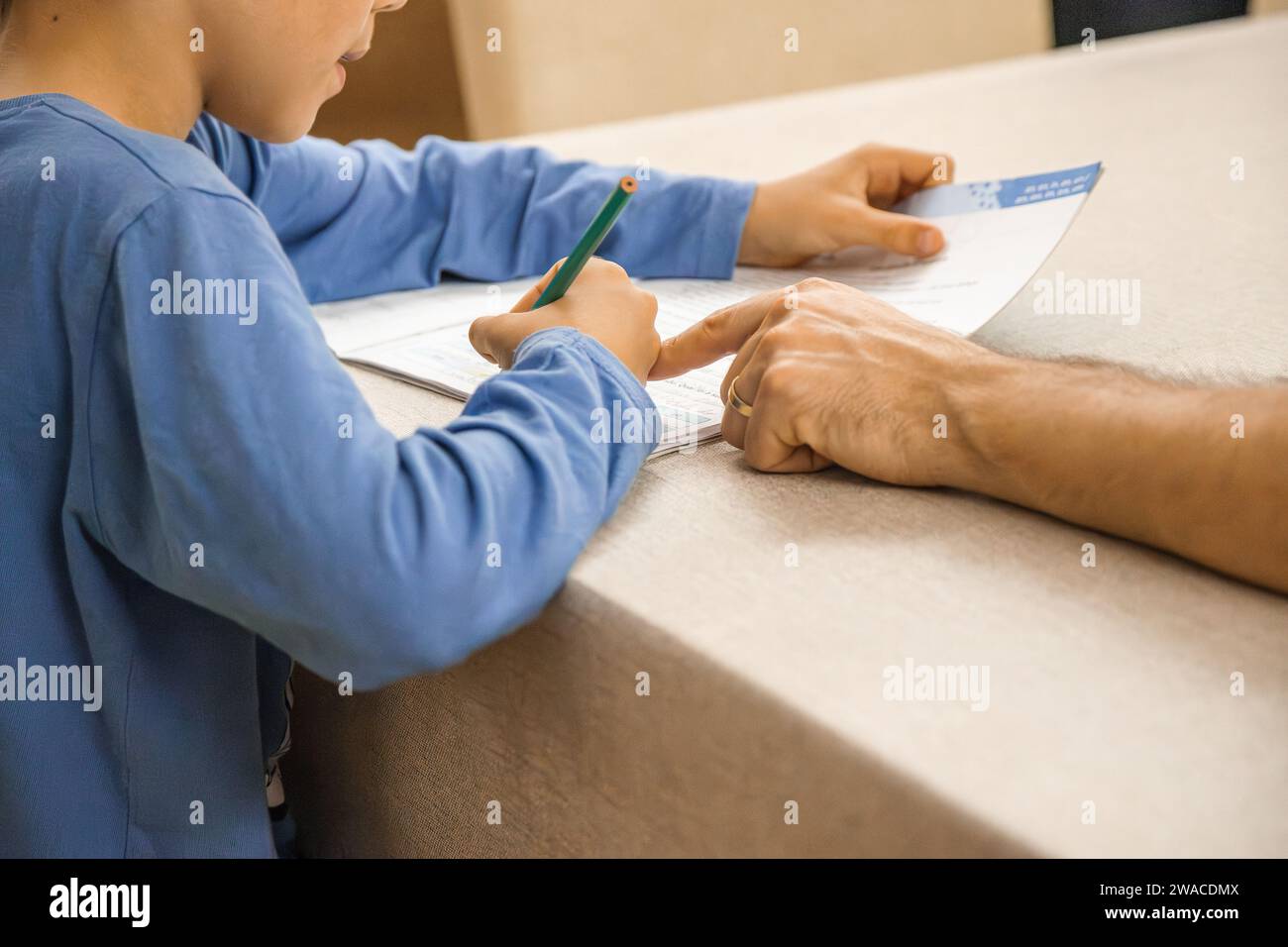 Kaukasisches Grundschulkind, das am Ende des Schultages mit elterlicher Hilfe und Unterstützung Hausaufgaben macht. Nahaufnahme und Kopierbereich. Stockfoto