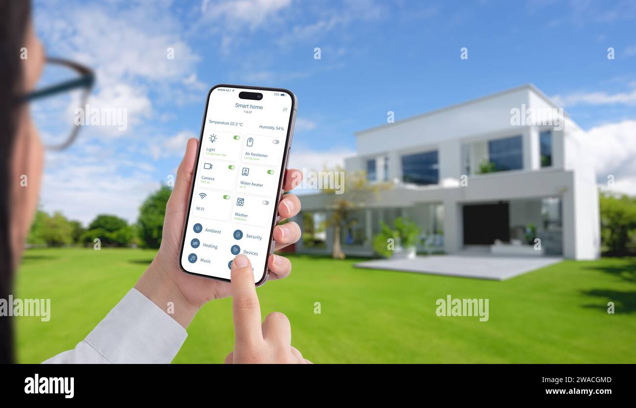 Frau steuert Temperatur und Heimgeräte mit einer Smart Home App. Modernes, umweltfreundliches Haus mit grünem Hof im Hintergrund Stockfoto
