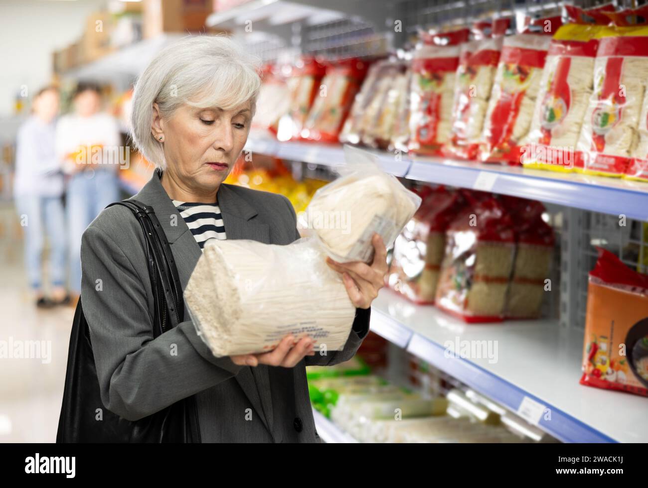 Interessierte Seniorin liest Etikett auf Verpackungen asiatischer Nudeln im Supermarkt Stockfoto