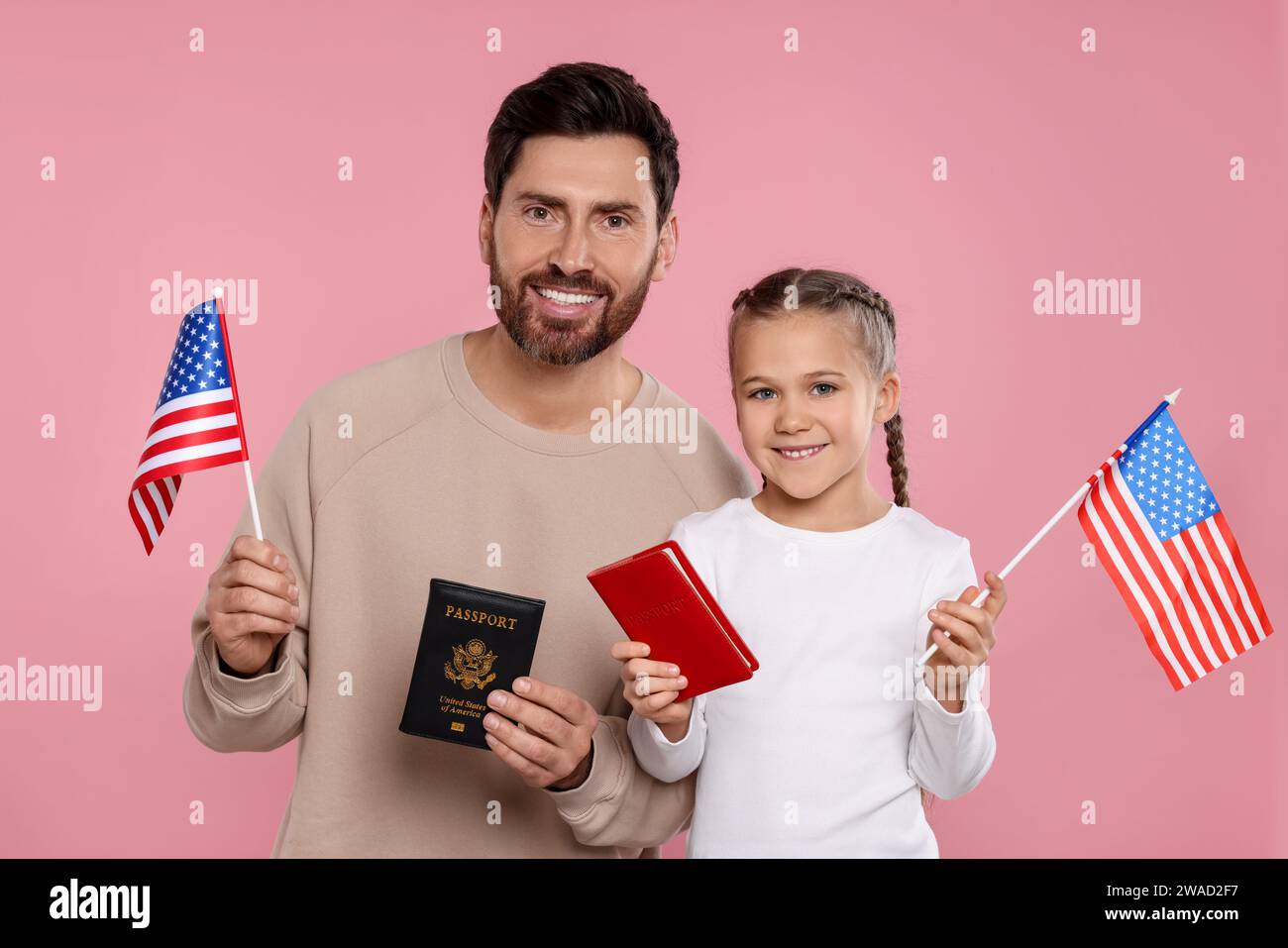 Einwanderung. Glücklicher Mann mit seiner Tochter, der Pässe und amerikanische Fahnen auf rosa Hintergrund hält Stockfoto