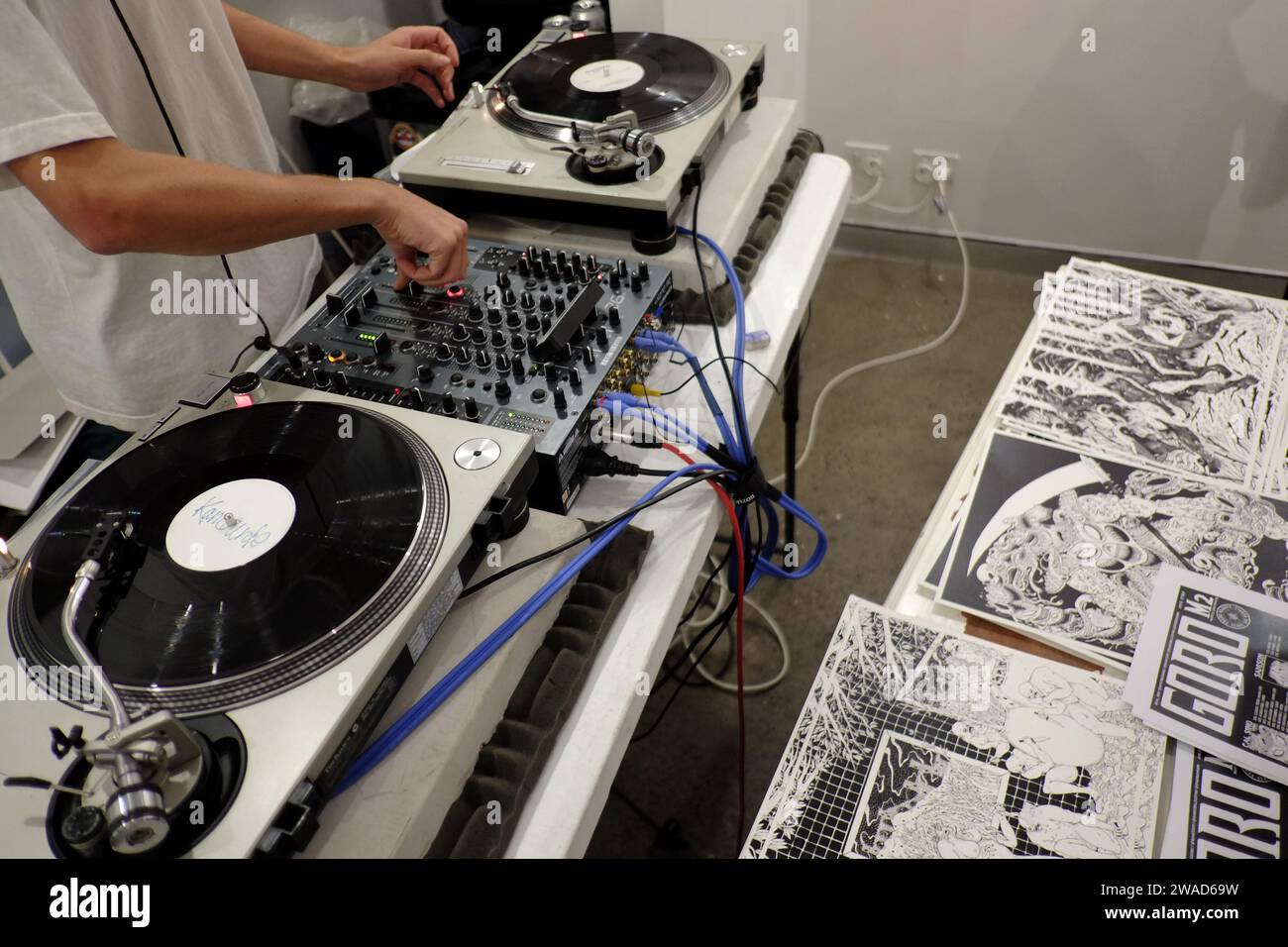 DJ arbeitet auf den Decks, dreht Vinyl in der M2 Art Gallery für eine Graphic Art und Zines (am Tisch) Eröffnungsabend und -Party Stockfoto