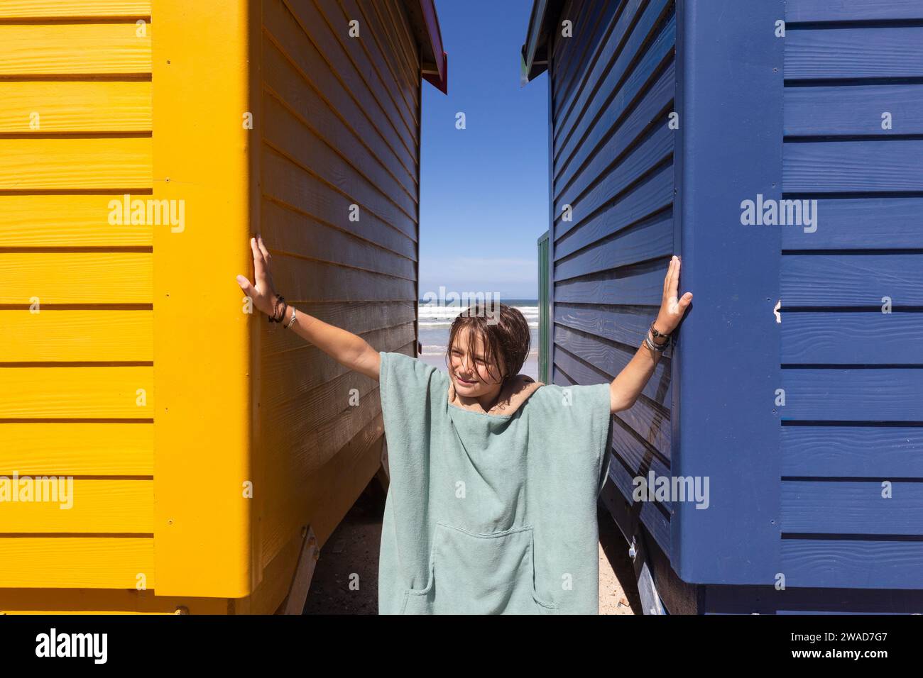 Junge (10-11) posiert vor der bunten Strandhütte am Muizenberg Beach Stockfoto