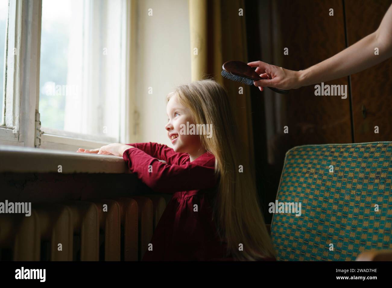 Mädchen (4-5) schaut durch das Fenster, während die Mutter ihre Haare putzt Stockfoto