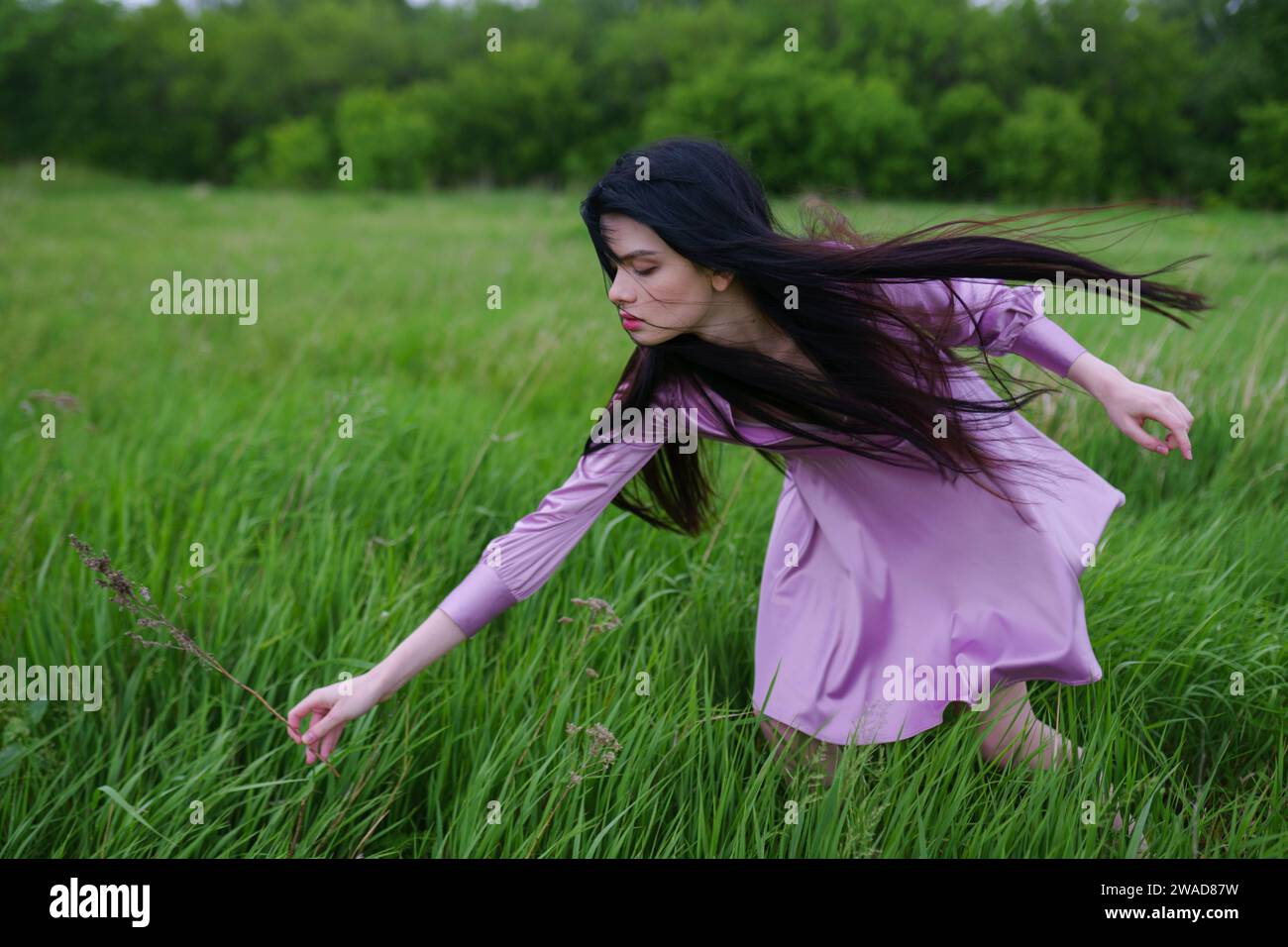 Porträt einer jungen Frau, die auf der Wiese Gras pflückt Stockfoto