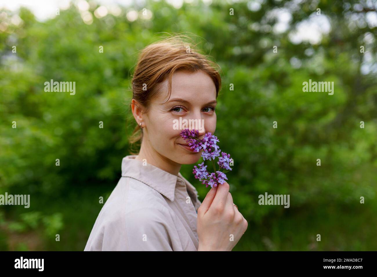Porträt einer lächelnden Frau, die Fliederblüte riecht Stockfoto