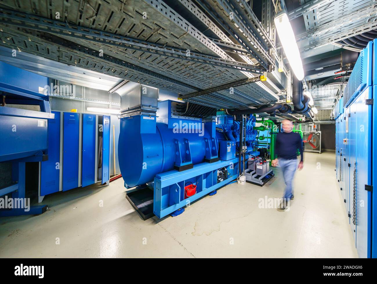 Offenbach, Deutschland. Dezember 2023. Ein Mitarbeiter geht an den Diesel-Notgeneratoren vorbei. Der Deutsche Wetterdienst (DWD) betreibt seit 1966 ein eigenes Computerzentrum. Das DWD-Mainframe-Rechenzentrum wird für die sehr rechenintensiven Wettervorhersagen genutzt und benötigt alle fünf bis sieben Jahre komplett neue Hochleistungs-Computersysteme. Darlegung: Andreas Arnold/dpa/Alamy Live News Stockfoto
