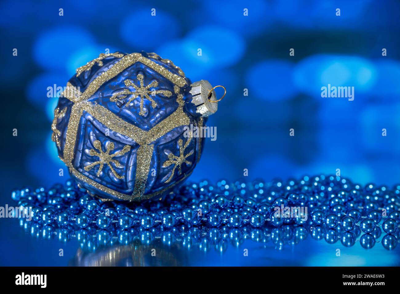 Eine blau-goldene Weihnachtsbaumkugel, fotografiert mit einer blauen Perlenkette auf blauem Hintergrund Stockfoto