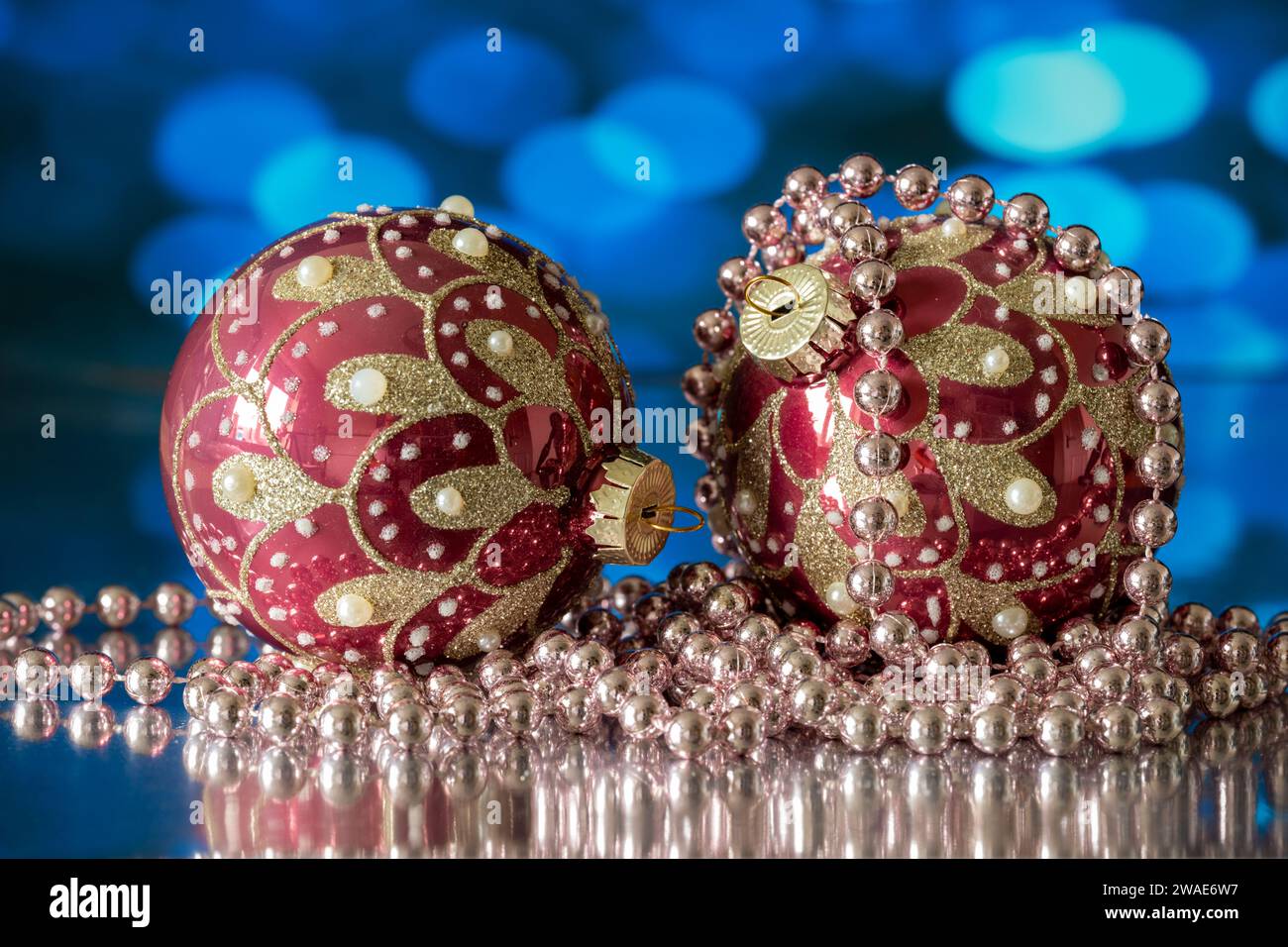 Ein Paar rote und goldene Weihnachtsbaumkugeln, fotografiert mit einer weißen Perlenkette, auf blauem Hintergrund Stockfoto