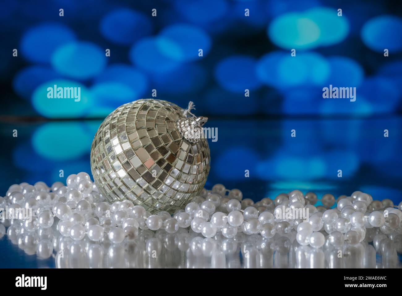 Eine Weihnachtsbaumkugel in Form eines Glitterballs, fotografiert mit einer weißen Perlenkette, auf blauem Hintergrund Stockfoto