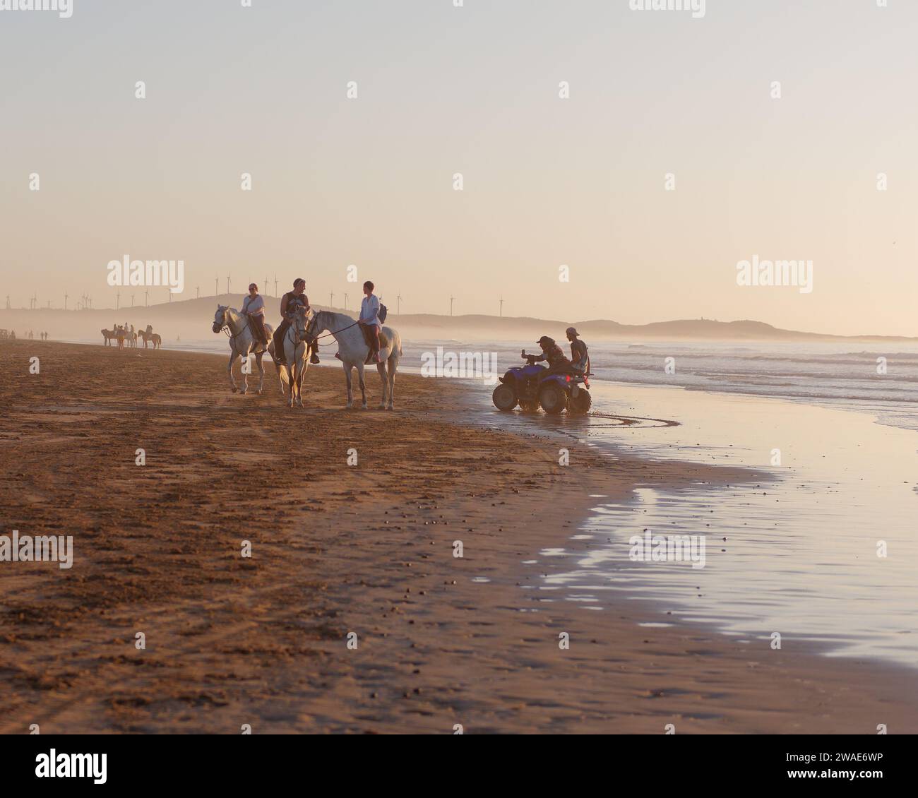 Personen auf Quad-Bikern filmen Pferdereiter an einem Strand, der sich dem Sonnenuntergang nähert, in Essaouira, Marokko, 3. Januar 2024 Stockfoto