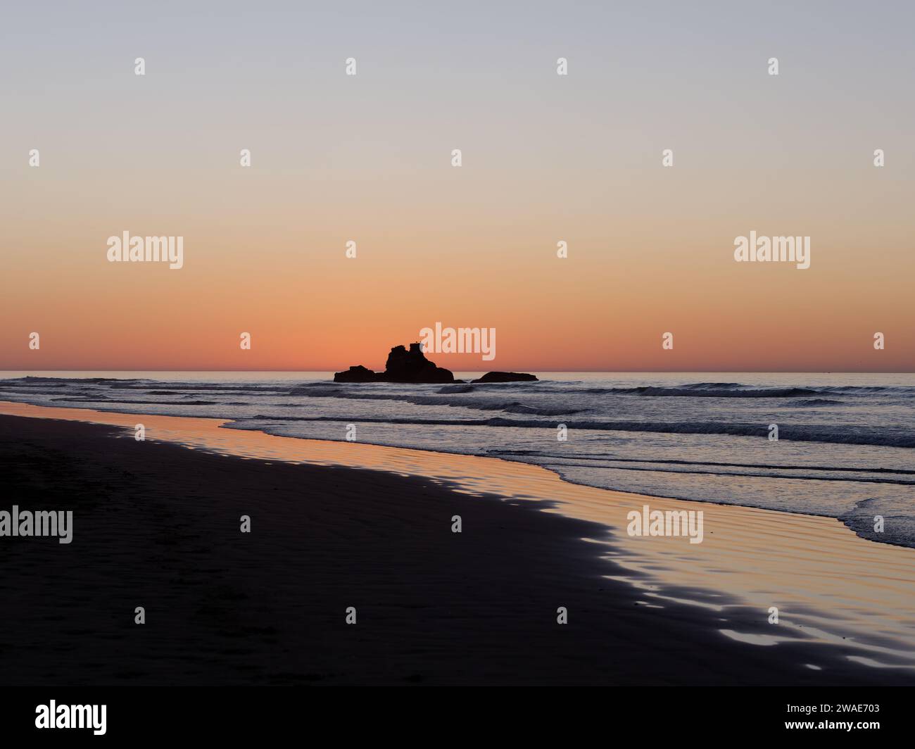 Felsvorsprung direkt vor der Küste zur goldenen Stunde, während das orange Licht im Wasser in der Stadt Essaouira, Marokko, am 3. Januar 2024 reflektiert wird Stockfoto