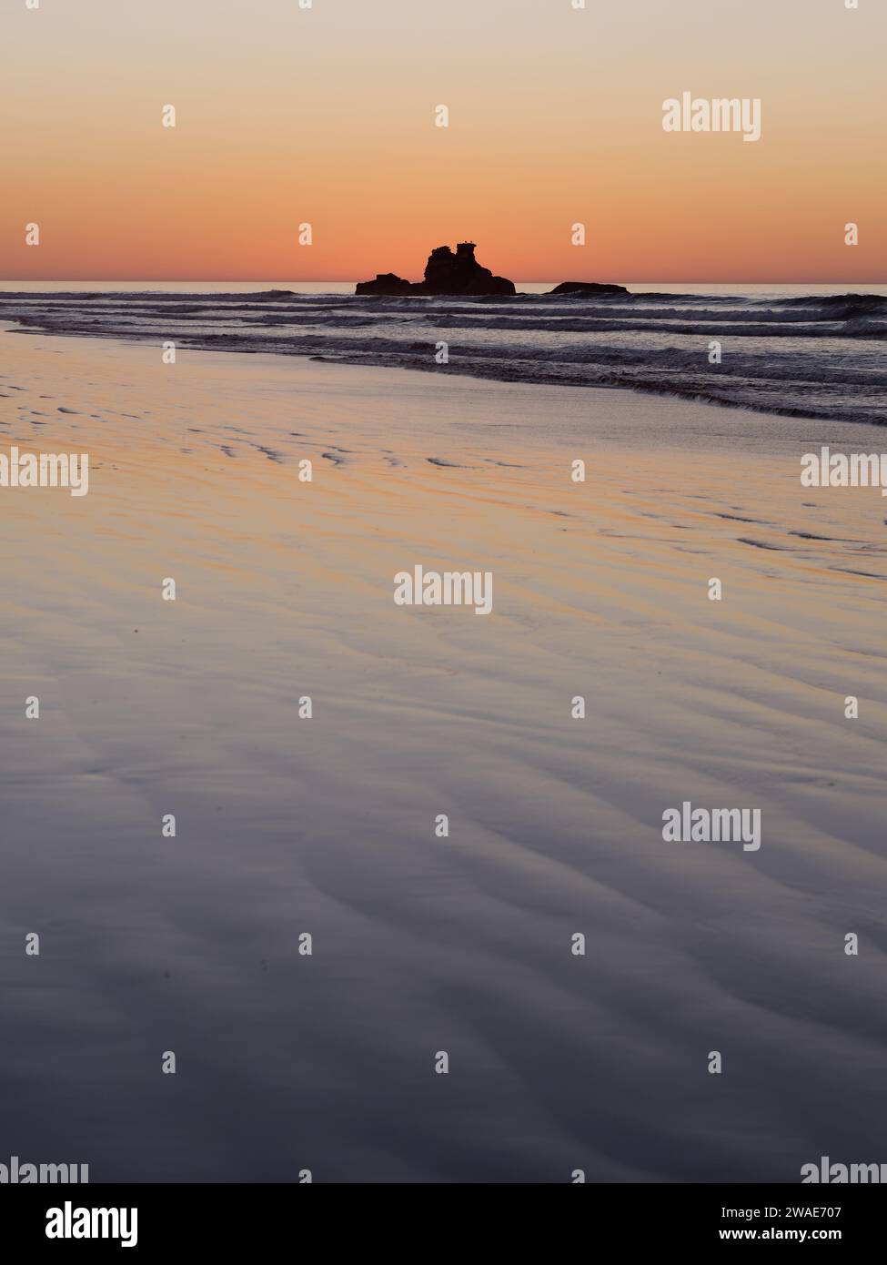 Felsvorsprung direkt vor der Küste zur goldenen Stunde, während das orange Licht im Wasser in der Stadt Essaouira, Marokko, am 3. Januar 2024 reflektiert wird Stockfoto