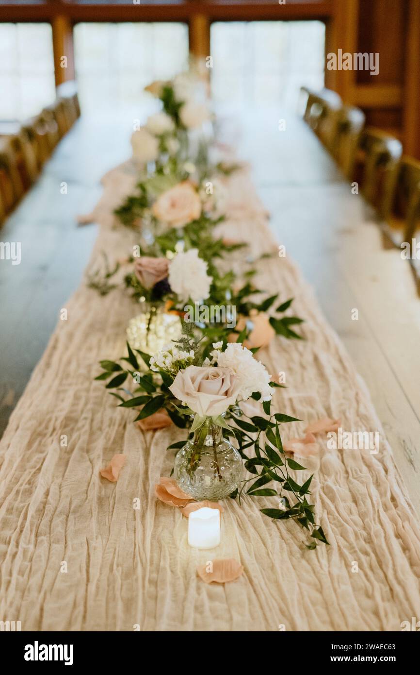 Ein rechteckiger Holztisch mit weißen Kerzen und frischen Blumenarrangements Stockfoto