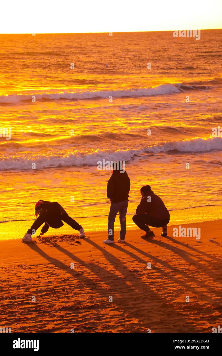 3 Jungs spielen am Strand, Silhouette, Meer, Sonnenuntergang Stockfoto