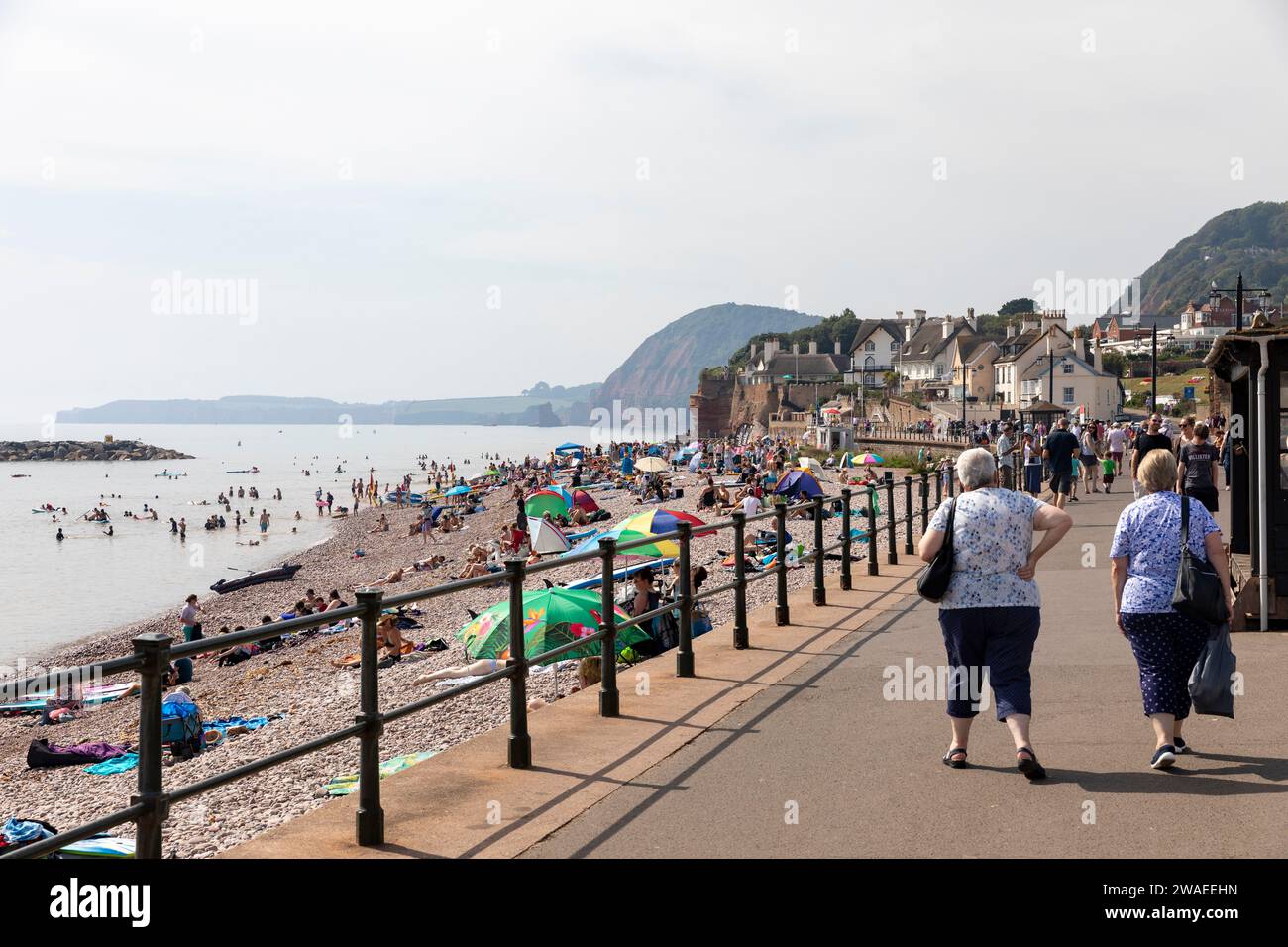 Sidmouth Devon, England, zwei ältere Frauen spazieren entlang der Esplanade von Sidmouth, während sich die Leute am Strand entspannen, heißer September 2023, Großbritannien Stockfoto
