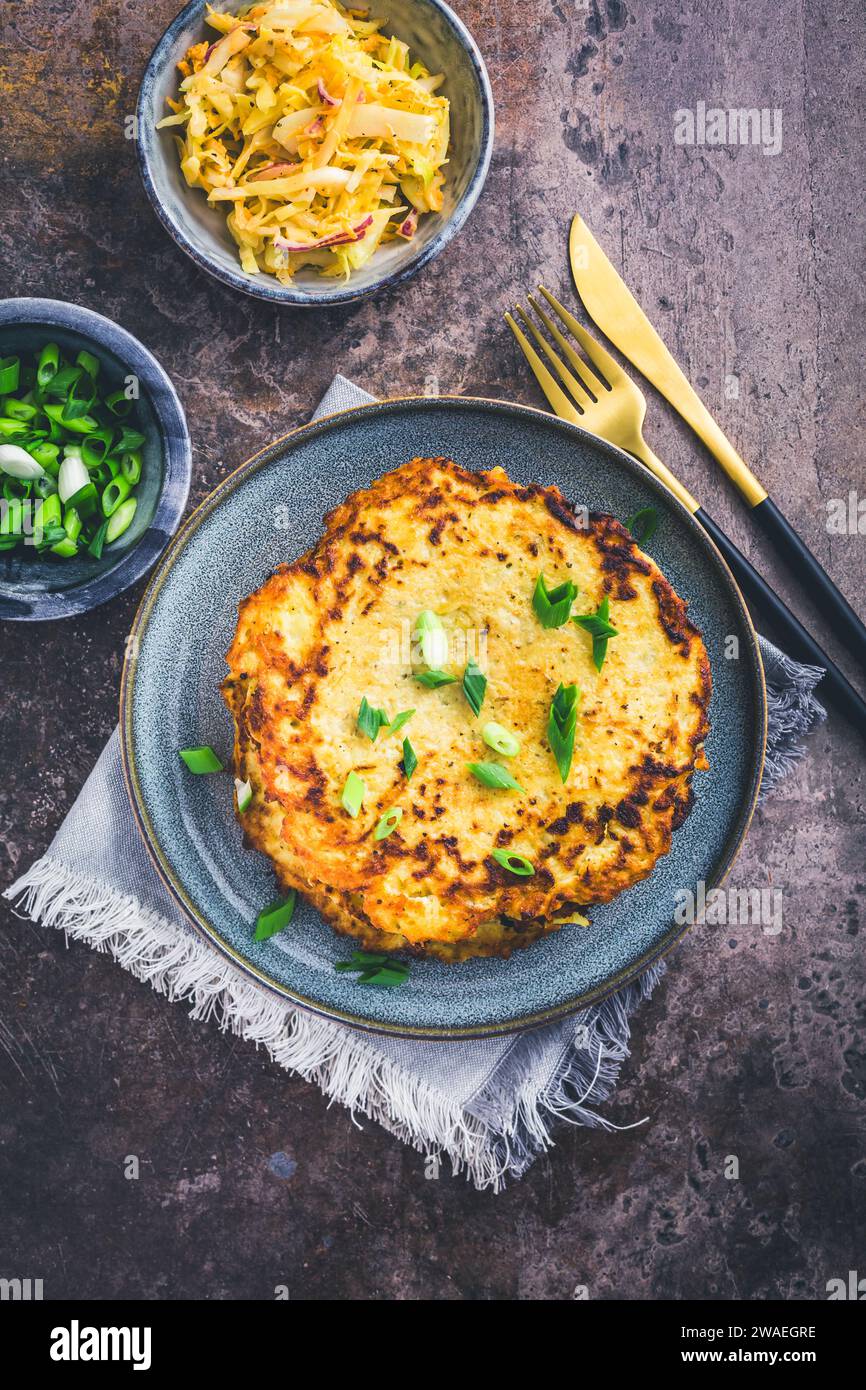 Hausgemachte Kartoffelrösti oder Kartoffelpfannkuchen mit Kohl-Salat und grünen Zwiebeln Stockfoto