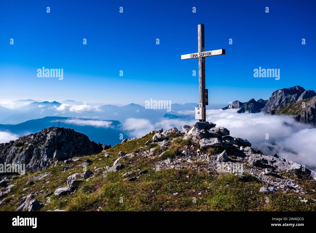 Das Kreuz auf dem Gipfel der Cima Sophia, Croz dell'Altissimo (links) und Cima Ghez (rechts) in der Ferne. Stockfoto