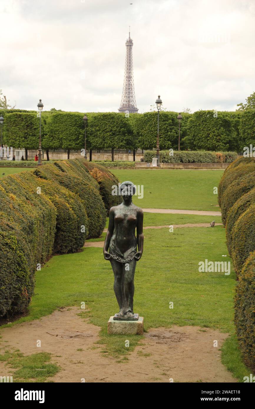 Eine majestätische Bronzestatue steht hoch vor einer üppig grünen Hecke mit dem berühmten Eiffelturm im Hintergrund Stockfoto