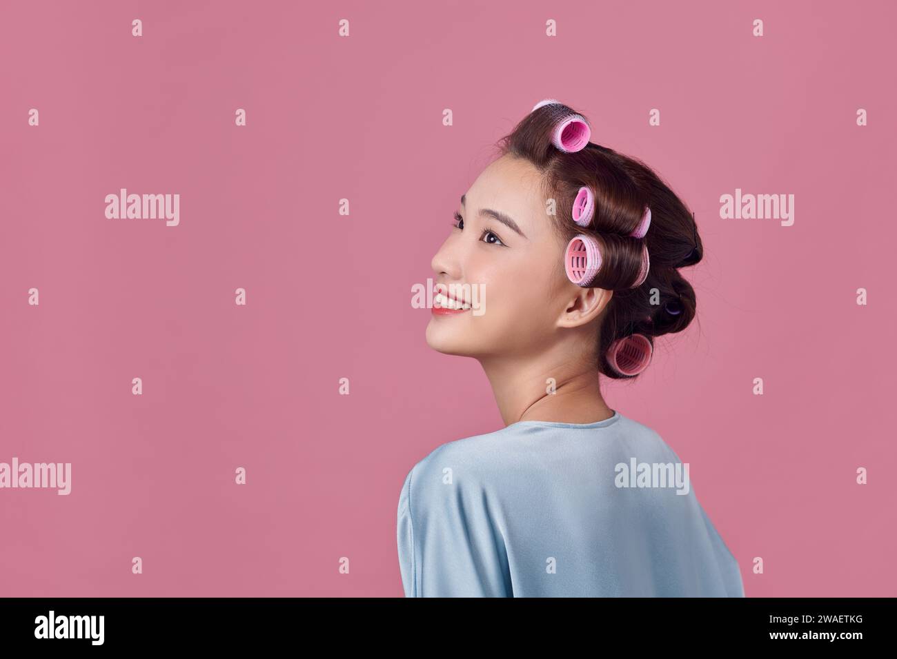 Junge Frau ist während des Tragens Lockenwickler, isoliert über weißen Tagträumen Stockfoto