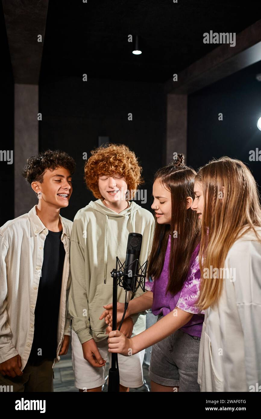 Fröhliche, talentierte Teenager-Jungen und -Mädchen singen zusammen und lächeln im Studio, in der Musikgruppe Stockfoto