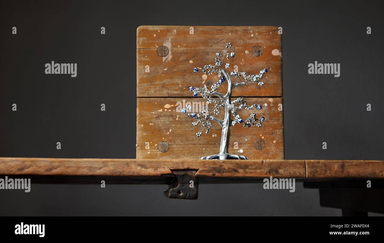 Eine künstlerische Komposition aus rustikalen schäbigen Holzmöbeln. Ein silberfarbener Souvenirbaum, Symbol für das türkische Auge. Leeres Holzbrett. Kopierbereich Stockfoto
