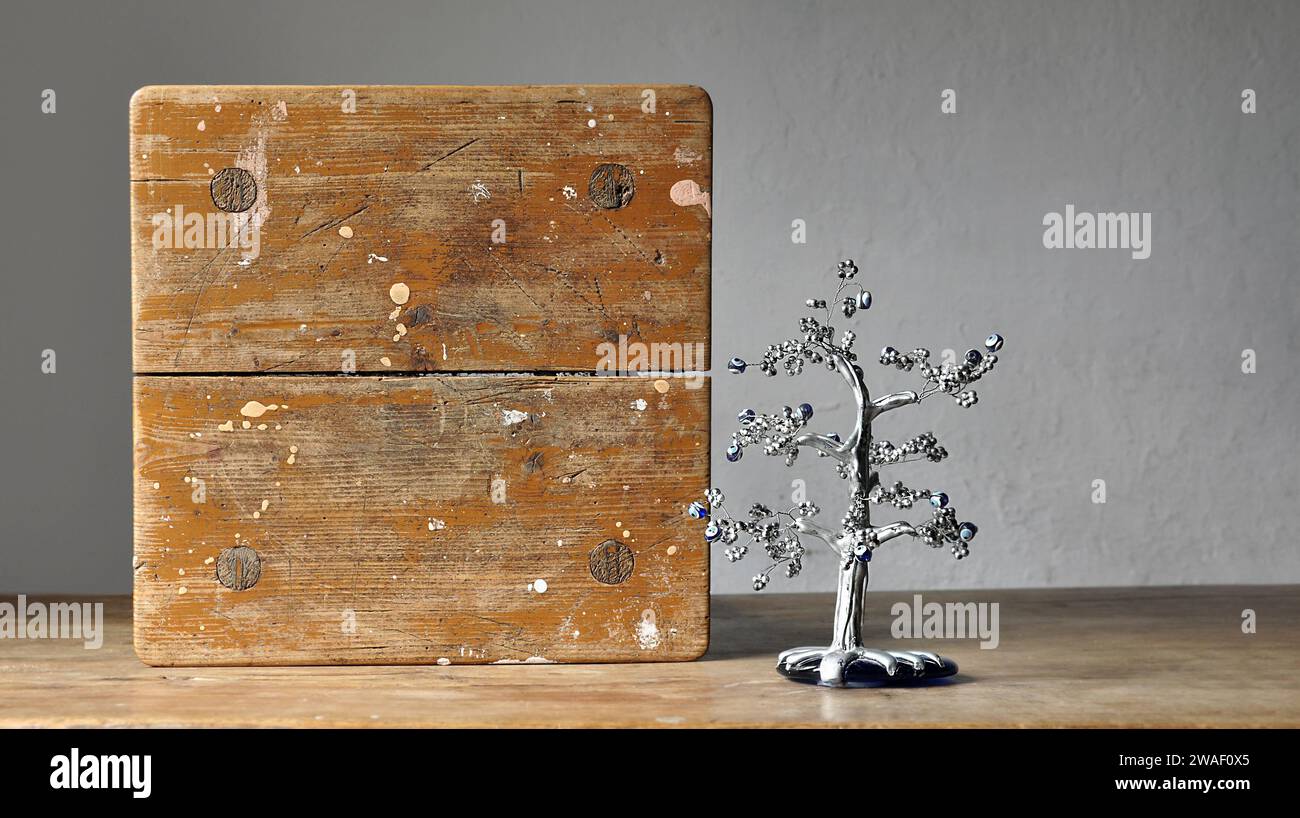 Eine künstlerische Komposition aus rustikalen schäbigen Holzmöbeln. Ein silberfarbener Souvenirbaum, Symbol für das türkische Auge. Leeres Holzbrett. Kopierbereich Stockfoto