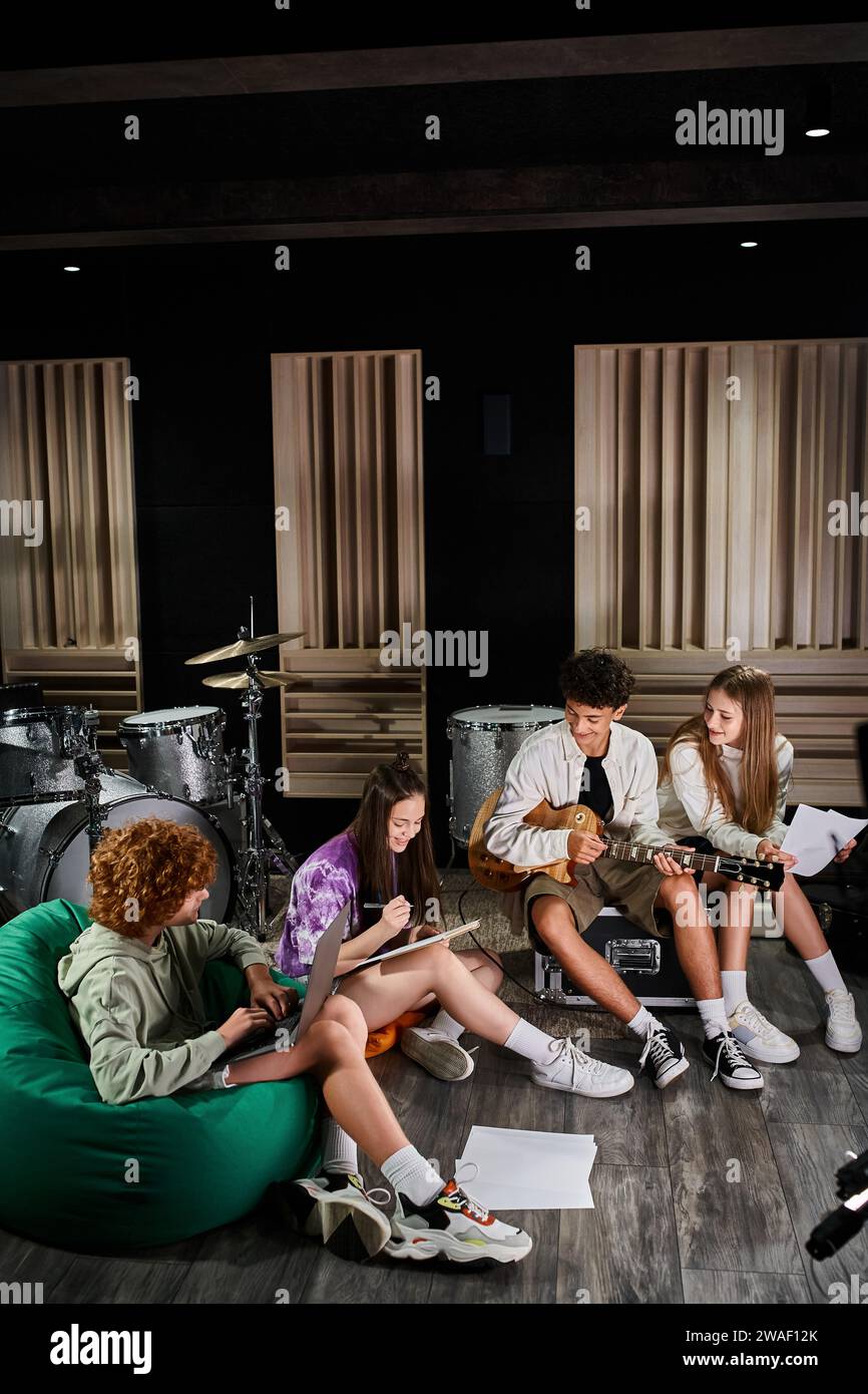 Fröhliche, entzückende Teenager-Jungen und -Mädchen sitzen im Studio mit Laptop und Gitarre und schreiben Texte Stockfoto