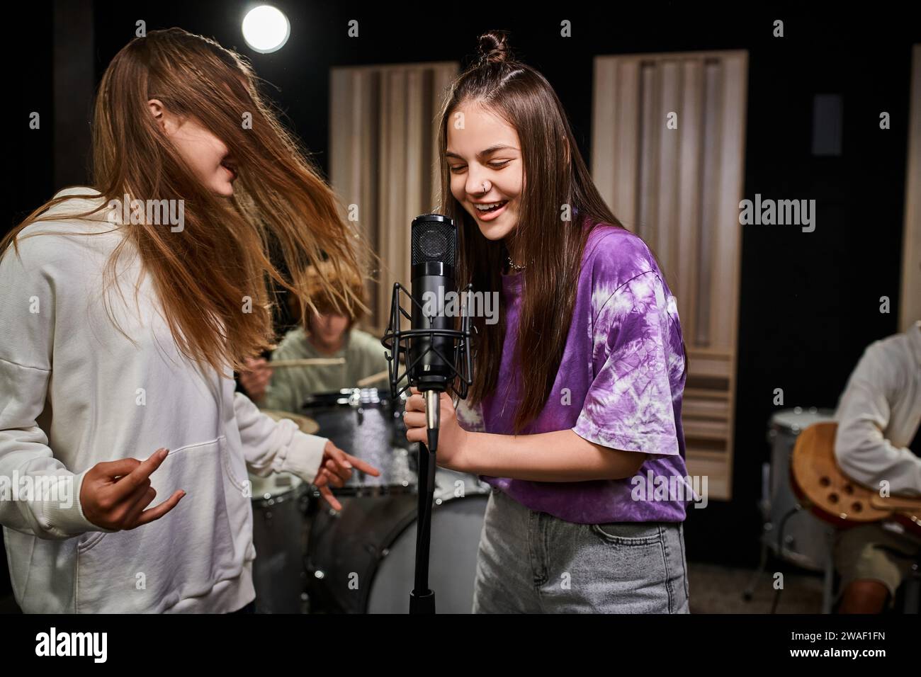 Entzückende, fröhliche Teenager-Mädchen singen und Rock-Zeichen zeigen, während Jungen verschiedene Instrumente spielen Stockfoto