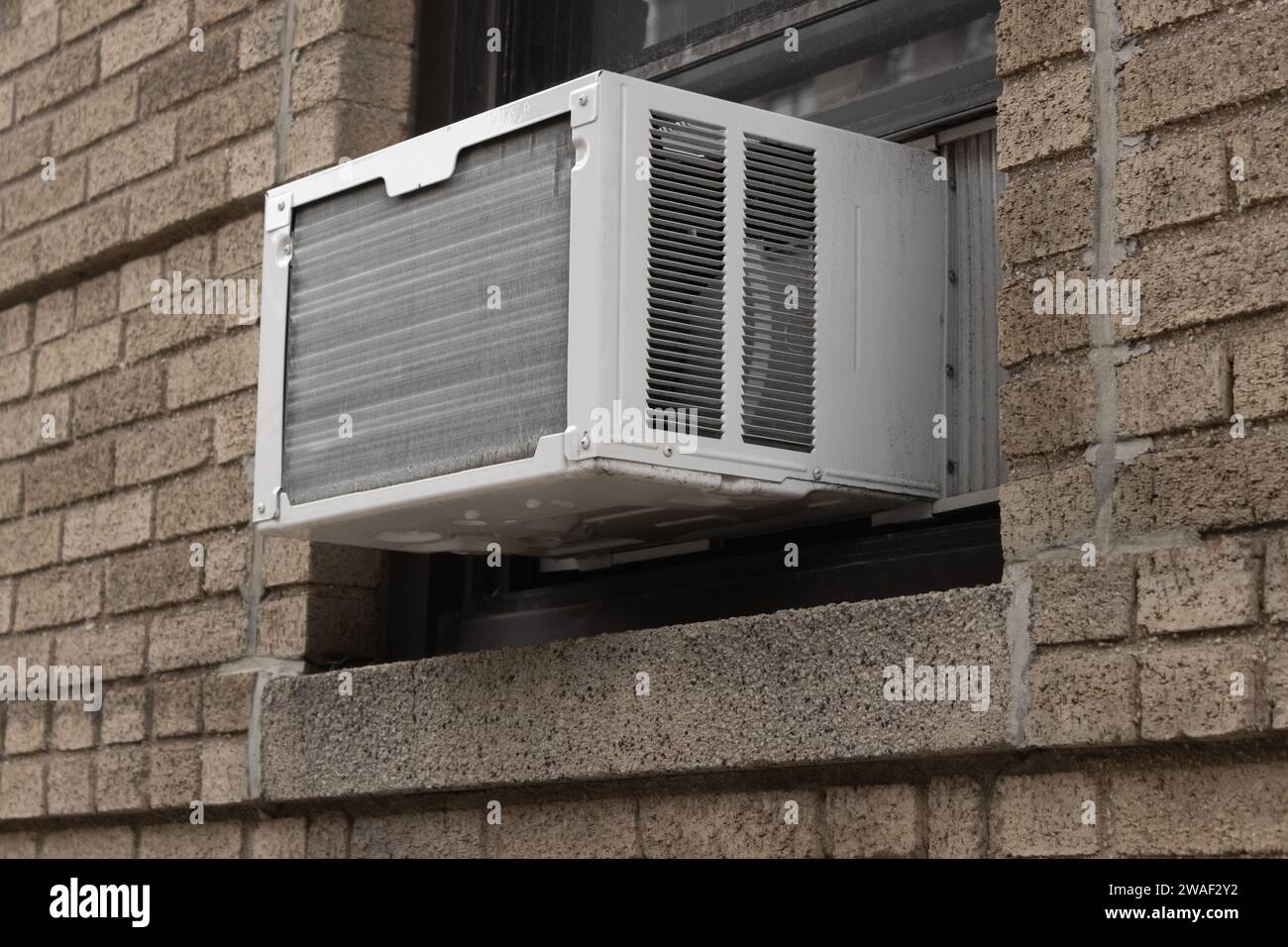 Außenansicht der Klimaanlagen-Fenstereinheit, die von der Fensterbank eines braunen Ziegelgebäudes aus extrudiert wird Stockfoto