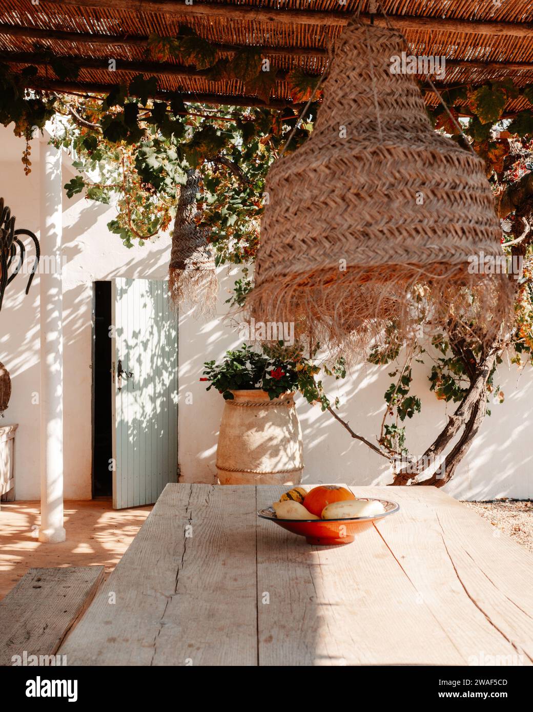 Ein hölzerner Außentisch mit einer rustikalen weißen Rattanlampe befindet sich in einem Garten eines traditionellen Landhauses Stockfoto