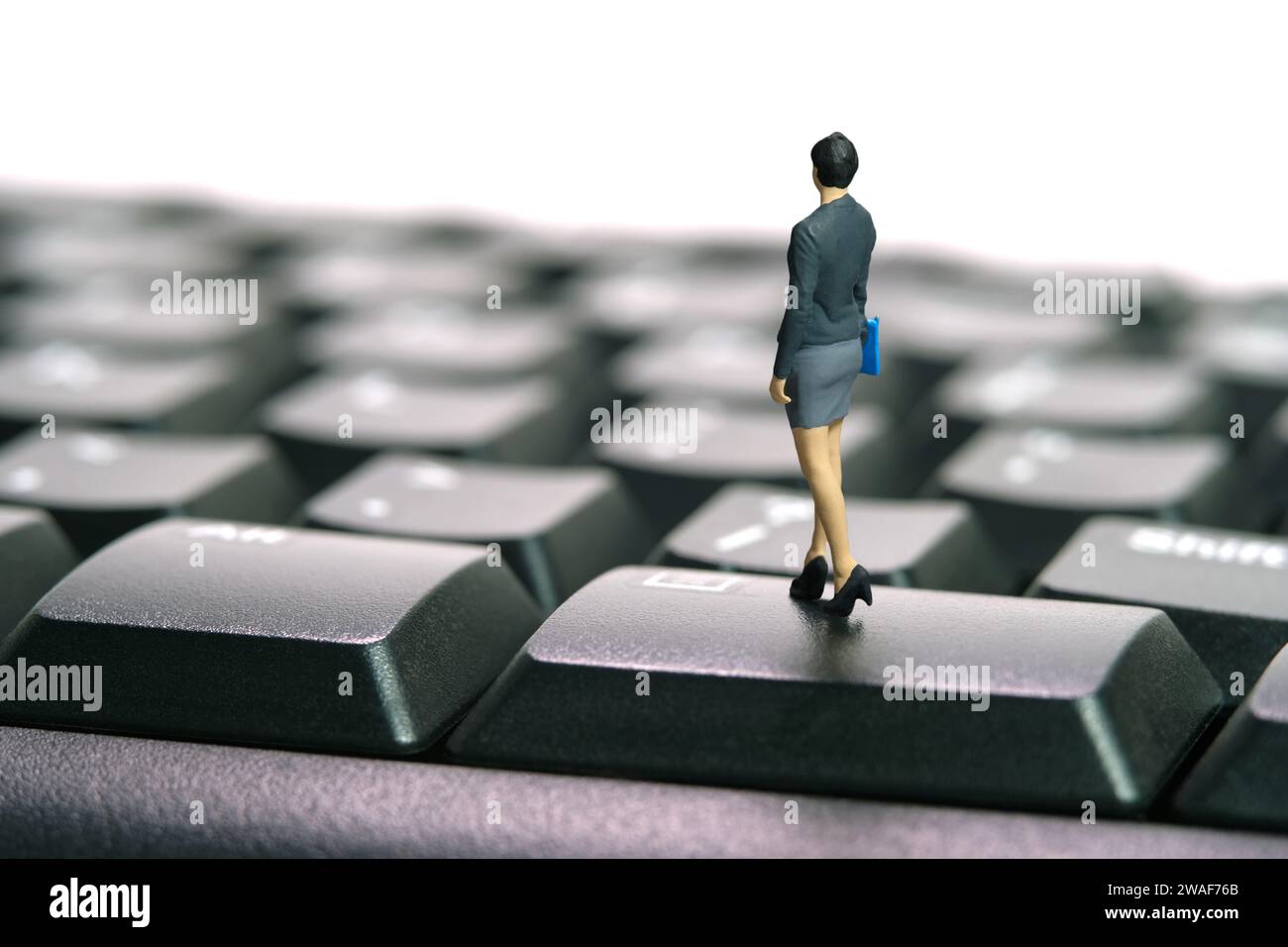 Miniatur Menschen Spielzeug Figur Fotografie. Jobkonzept eingeben. Eine Geschäftsfrau, die über der schwarzen Tastatur steht. Isoliert auf weißem Hintergrund. Bildfoto Stockfoto