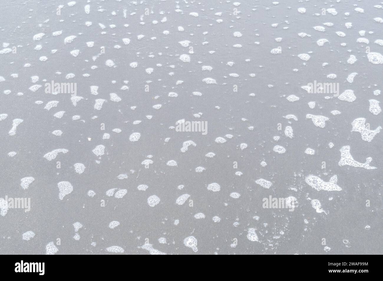 Unscharfe Fotos von grauer oder dunkler Sandoberfläche mit kleinen Schaumstoffen verteilen sich oben. Stockfoto