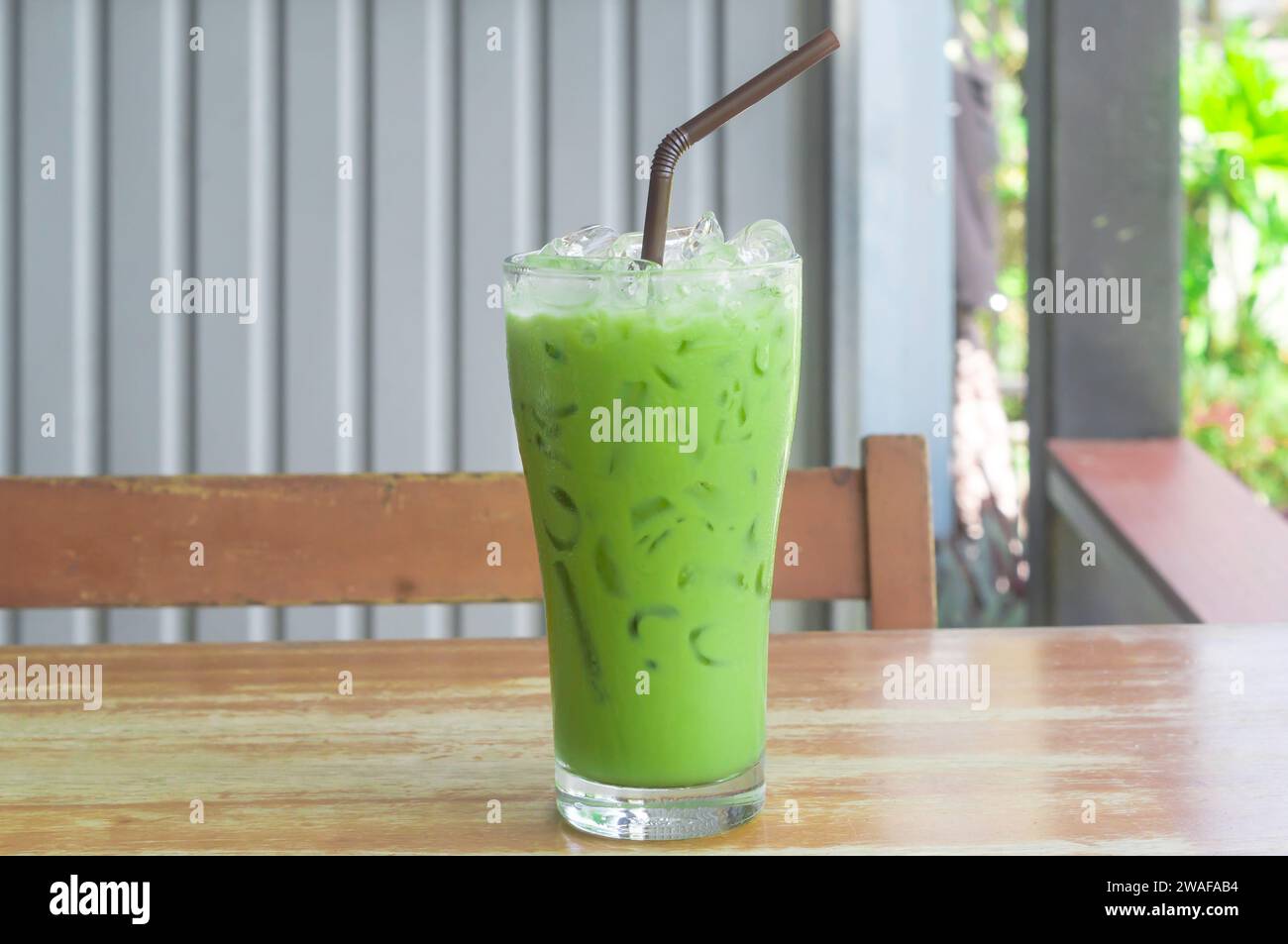 Eismatcha Latte oder grüner Tee mit Kondensmilch in transparentem Glas mit schwarzem Stroh auf Holztisch wird im Coffee Shop serviert. Stockfoto