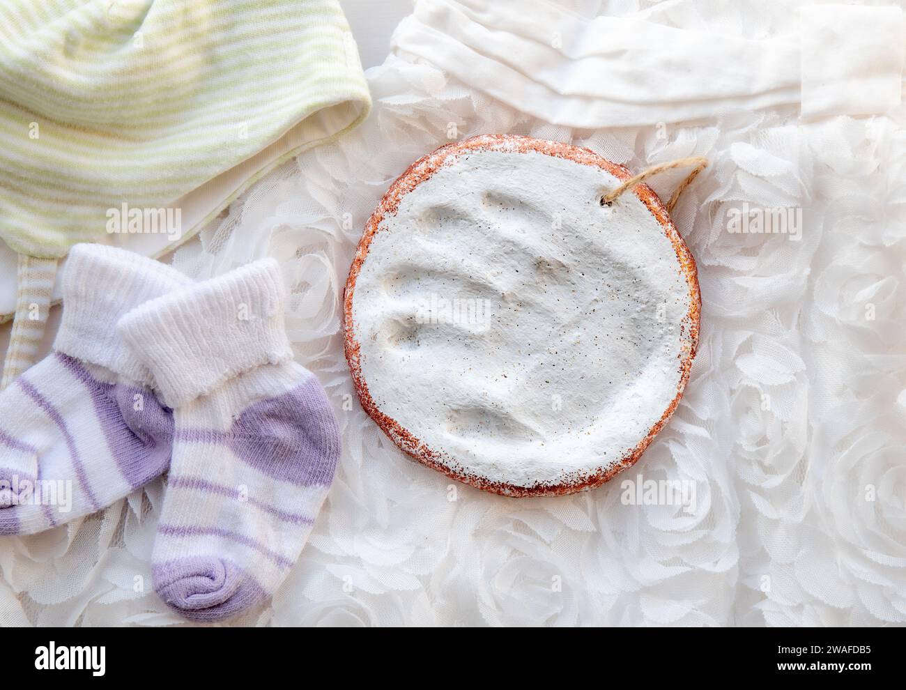 Handgefertigter, handgefertigter Baby-Druck in Ton zur Erinnerung. Weißer Handabdruck auf weißem Kleid und niedliche, winzige Socken Memrobilia im Wohnzimmer. Stockfoto