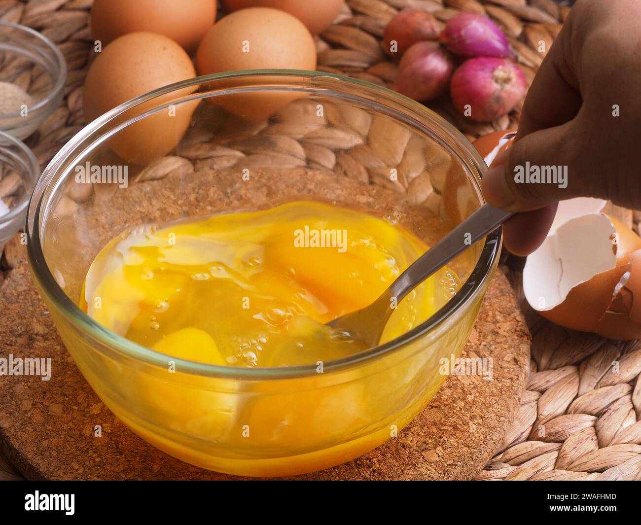 Die Eier in einer Glasschüssel mit einer Gabel von Hand mischen, als Hintergrundeier, rote Zwiebeln, Salz und Paprika verwenden Stockfoto