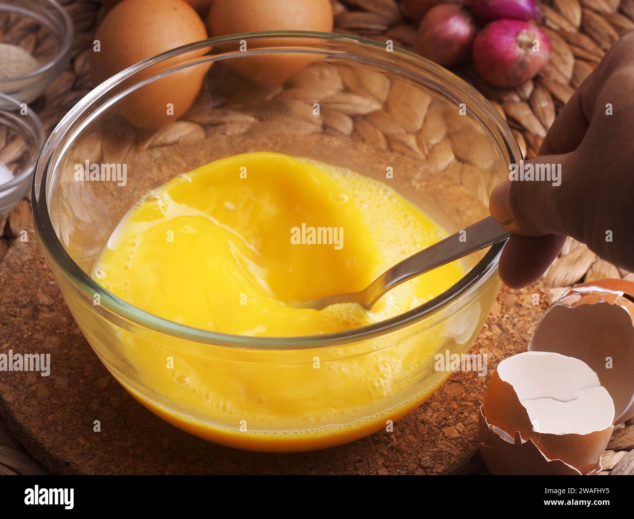 Die Eier in einer Glasschüssel mit einer Gabel von Hand mischen, als Hintergrundeier, rote Zwiebeln, Salz und Paprika verwenden Stockfoto