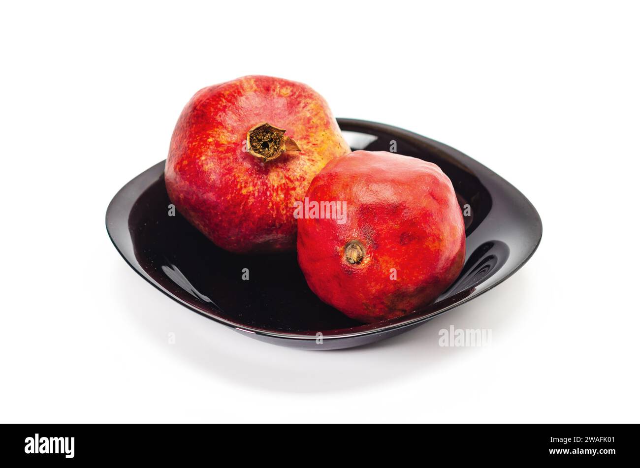 Zwei reife rote Granatäpfel in schwarzer Schüssel, isoliert auf weißem Hintergrund. Saftige Früchte. Stockfoto