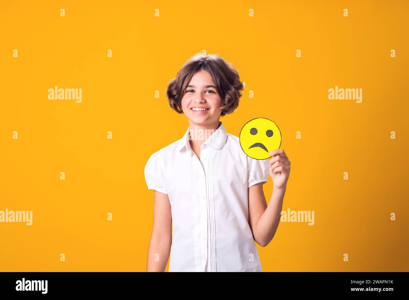 Mädchen lächelt und hält trauriges Emoticon. Psychische Gesundheit, Psychologie und kindliches Gefühlskonzept Stockfoto