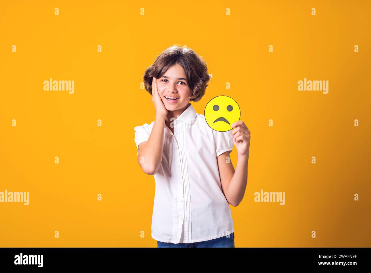 Mädchen lächelt und hält trauriges Emoticon. Psychische Gesundheit, Psychologie und kindliches Gefühlskonzept Stockfoto