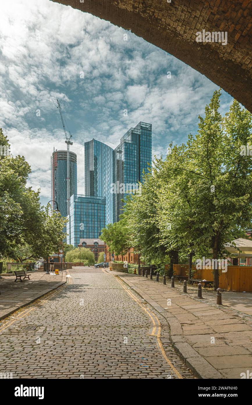 Eingerahmt von einer Eisenbahnbrücke erhebt sich die zeitgenössische Architektur der Wolkenkratzer von Manchester über traditionelleren Häusern. Stockfoto