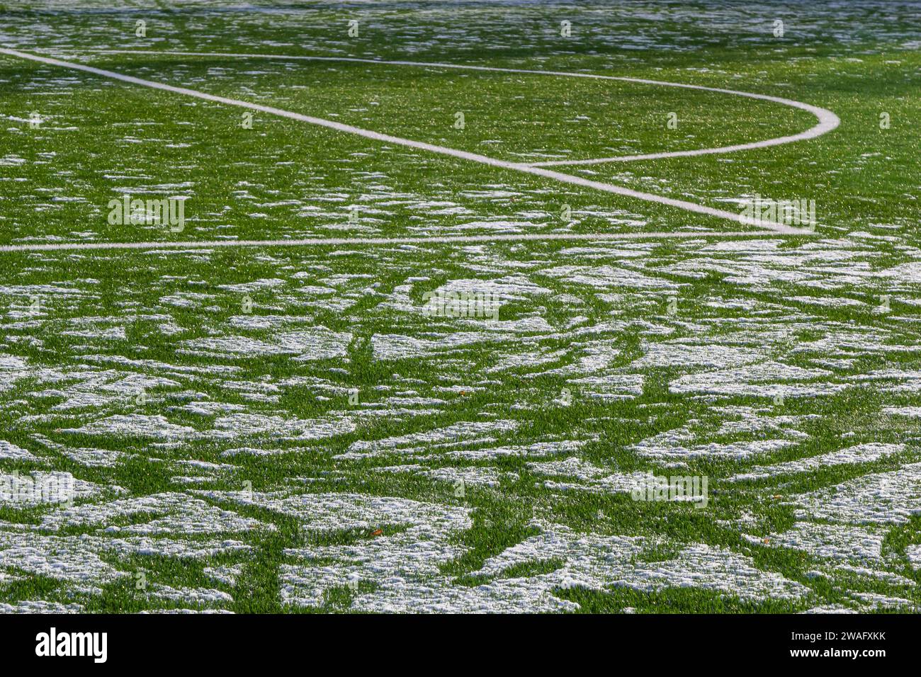 Das Fußballfeld mit Kunstrasen ist mit einer leichten Schneeschicht bedeckt. Frühling. Grünes Gras auf dem Fußballfeld ist von zu sehen Stockfoto