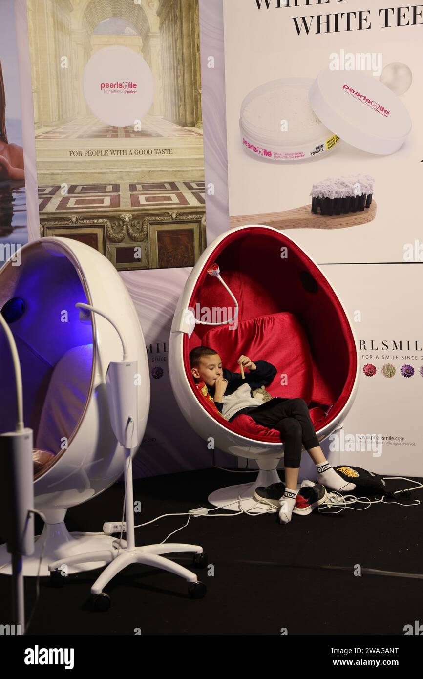 Kleiner Junge, der sich in einem eiförmigen Behandlungsstuhl von PearlSmile auf der Masters Expo in Amsterdam entspannt, mit ausziehenden Schuhen im Sackgasse sitzt Stockfoto