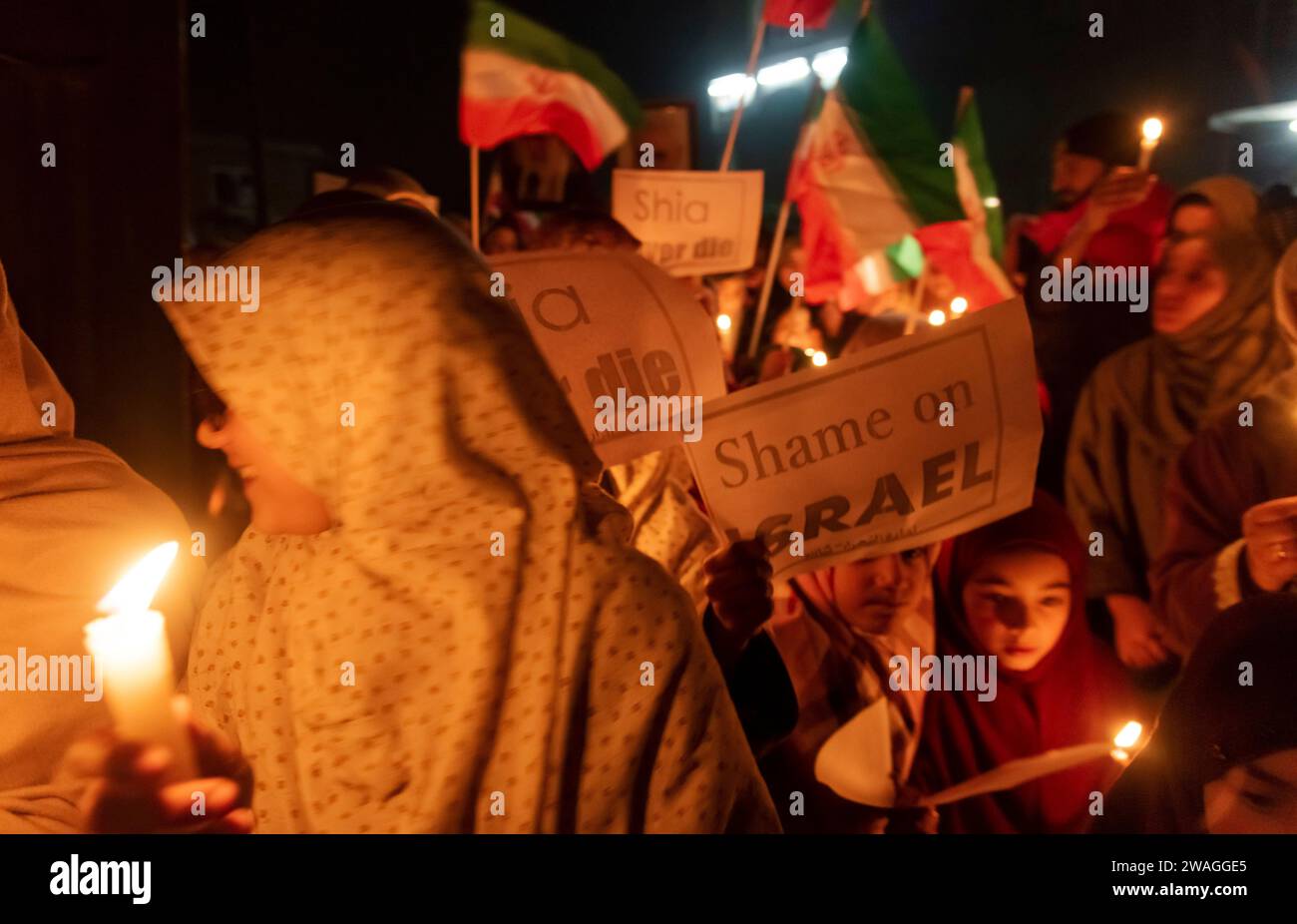 Kaschmiri schiitische Muslime halten Plakate und iranische Fahnen, während sie während einer Mahnwache bei Kerzenlicht Anti-Israel- und Anti-USA-Parolen rufen. Am Rande von Srinagar, Kaschmir, hielten schiitische Muslime aus der kaschmirischen Gemeinde eine Mahnwache bei Kerzenlicht ab, in der sie ihren Widerstand gegen Israel und die Vereinigten Staaten zum Ausdruck brachten. Die feierliche Versammlung nahm eine tragische Wende, als 84 Personen ihr Leben verloren und zahlreiche andere während einer Zeremonie zum Gedenken an den Tod des iranischen Generals Qassem Soleimani in einer Explosion verletzt wurden. Der Islamische Staat übernahm die Verantwortung für die beiden zerstörerischen Explosionen, die zur dea führten Stockfoto