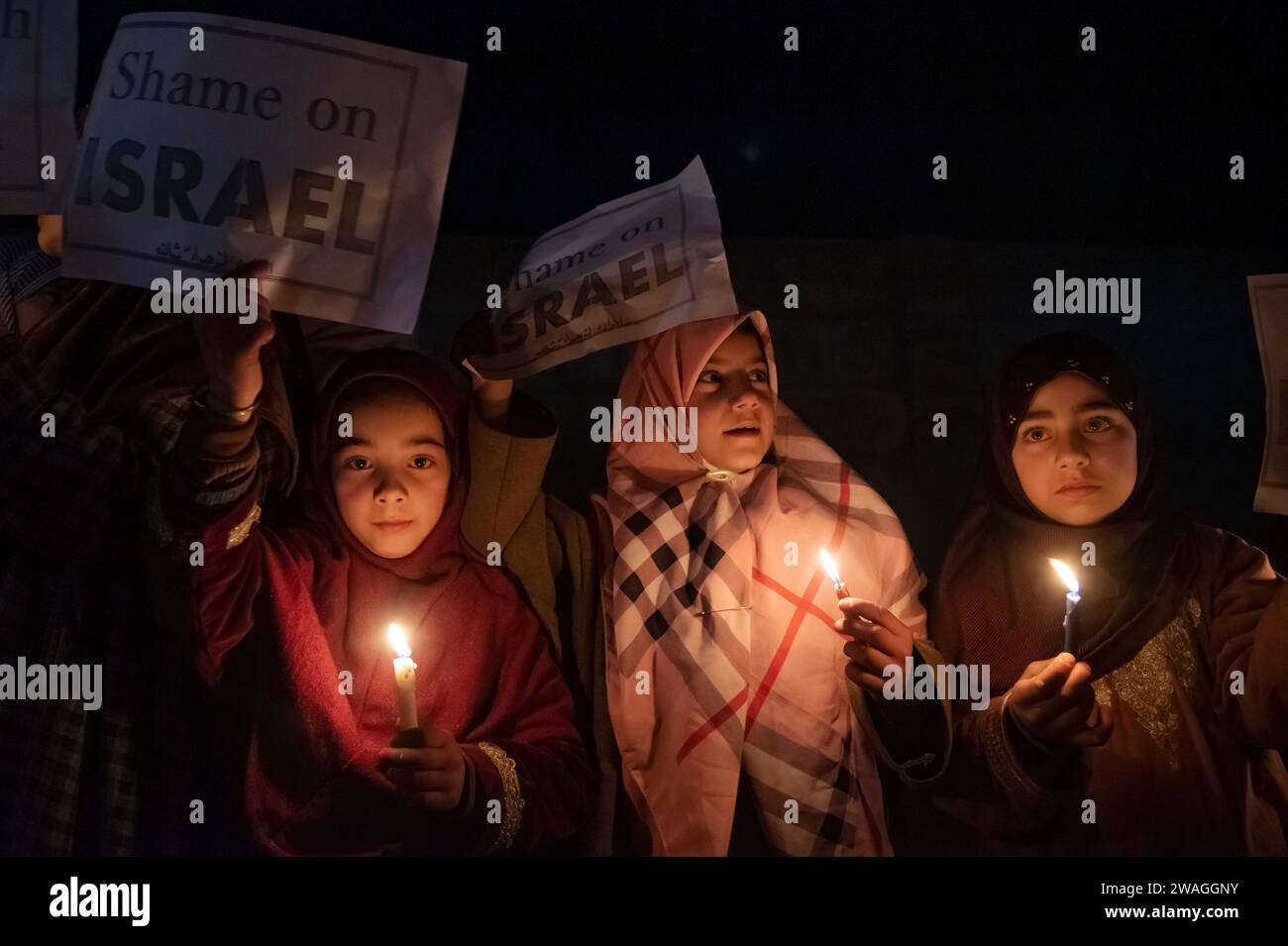 Kaschmiri schiitische Muslime halten während einer Mahnwache bei Kerzenlicht „Scham über Israel“-Plakate und -Kerzen. Am Rande von Srinagar, Kaschmir, hielten schiitische Muslime aus der kaschmirischen Gemeinde eine Mahnwache bei Kerzenlicht ab, in der sie ihren Widerstand gegen Israel und die Vereinigten Staaten zum Ausdruck brachten. Die feierliche Versammlung nahm eine tragische Wende, als 84 Personen ihr Leben verloren und zahlreiche andere während einer Zeremonie zum Gedenken an den Tod des iranischen Generals Qassem Soleimani in einer Explosion verletzt wurden. Der Islamische Staat übernahm die Verantwortung für die beiden zerstörerischen Explosionen, die den Tod von 84 Menschen während des Ereignisses zur Folge hatten Stockfoto