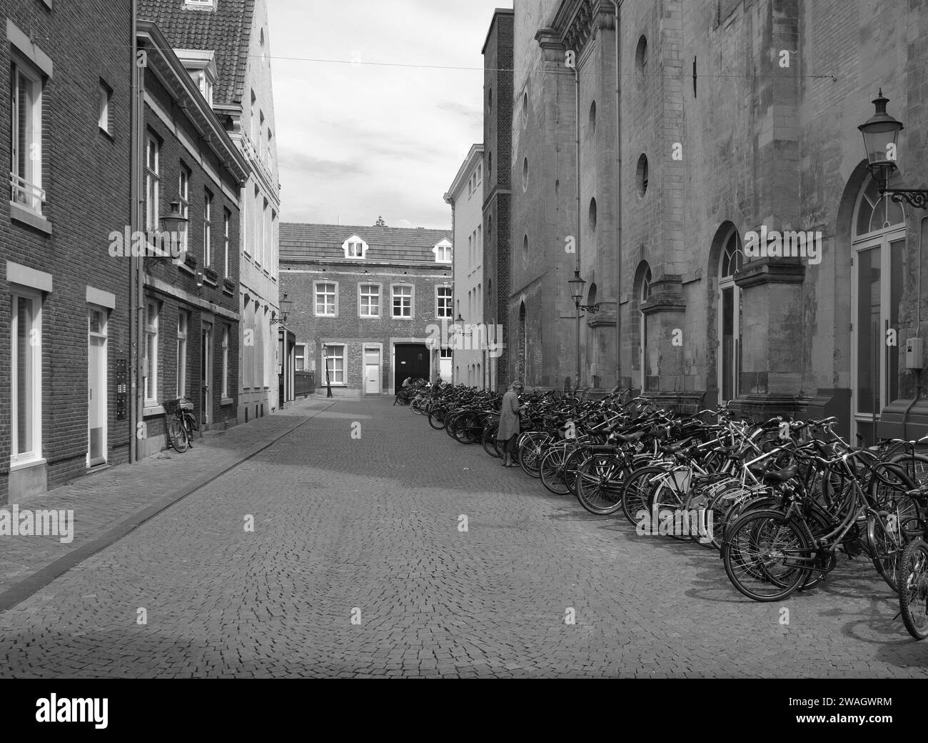 Maastricht, das niederländische Stadtzentrum mit alten historischen Gebäuden, Geschäften, Geschäften mit geparkten Fahrrädern in einer Reihe auf einer Kopfsteinpflasterstraße in Schwarzweiß Stockfoto
