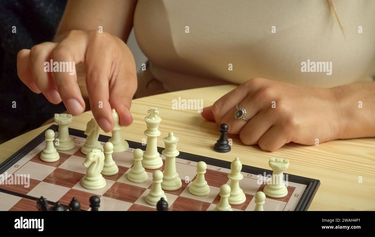 Schach wie ein Gehirnspiel, mit schwarzen und weißen Figuren auf dem Brett. Eine junge Frau sitzt am Schachtisch und bewegt sich. Stockfoto