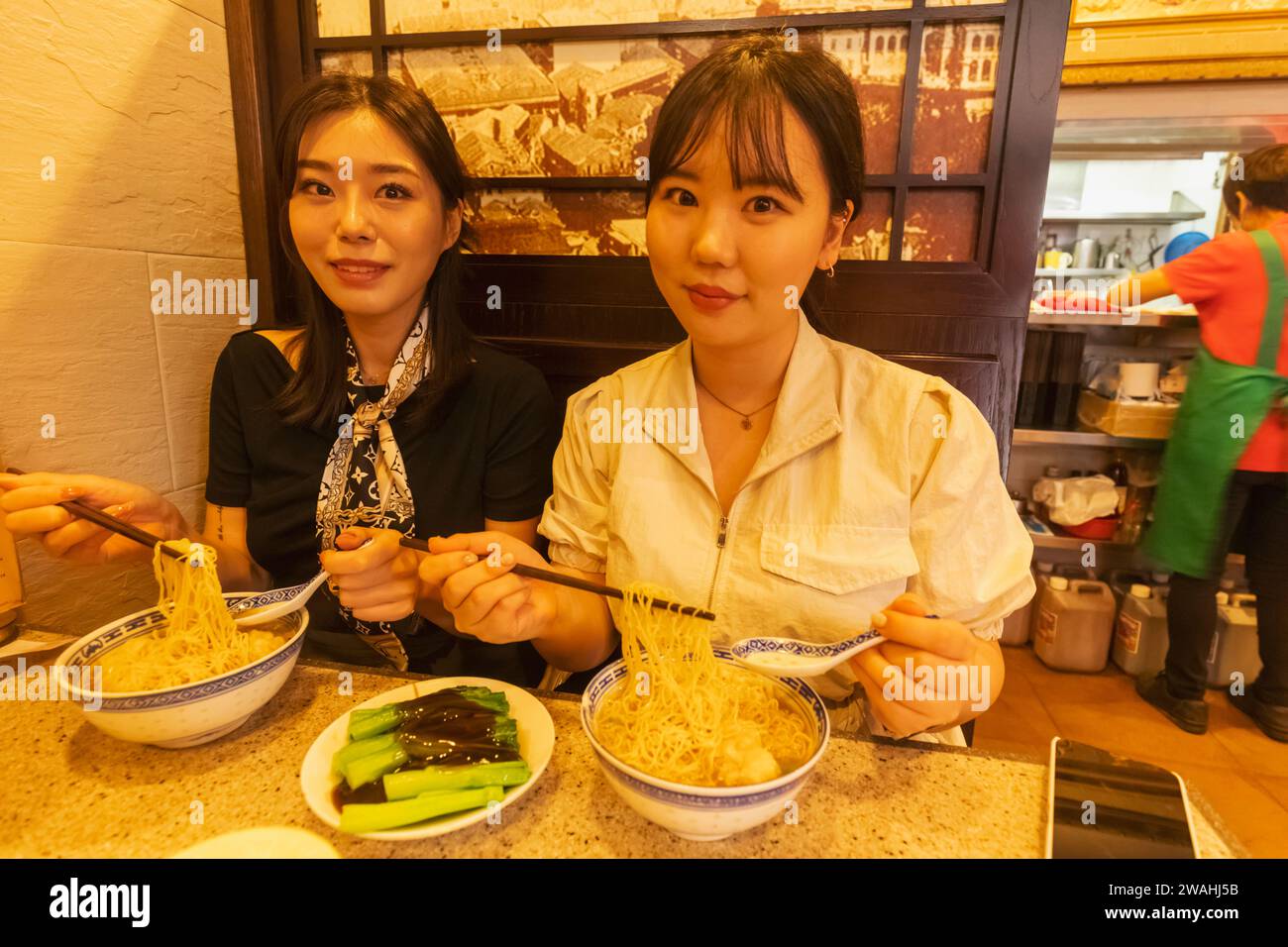 China, Hongkong, Hong Kong Island, Central, zwei junge asiatische Frauen essen Wonton Nudeln mit Essstäbchen Stockfoto