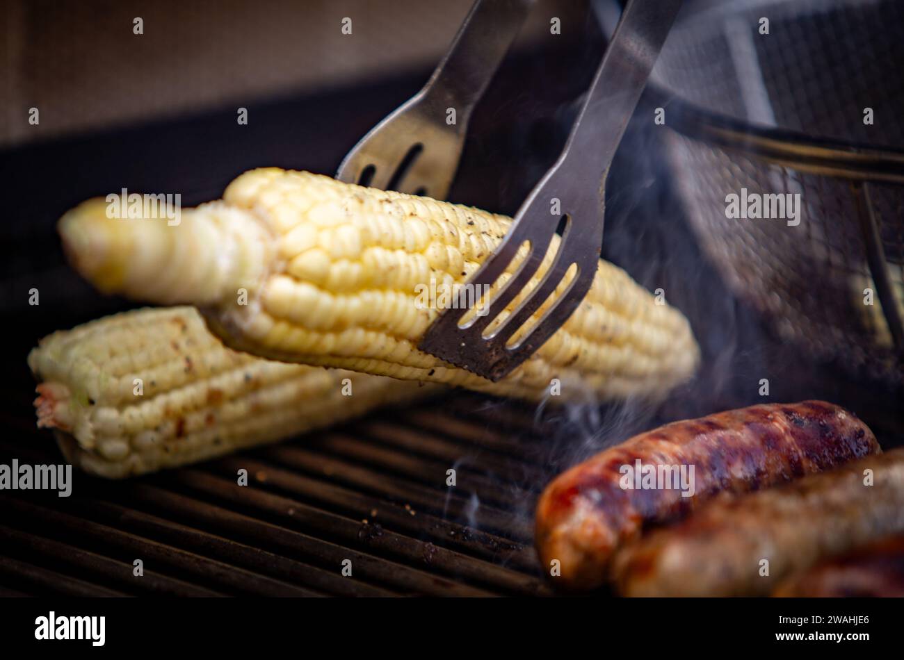 Greifen Sie Mais auf dem Grill, während Würstchen gekocht werden Stockfoto