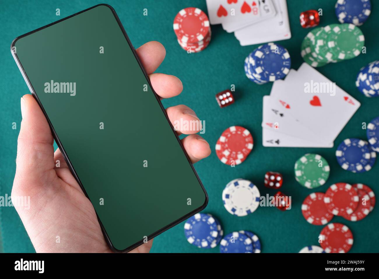Konzept des Spielens von Online-Casino-Spielen mit Handheld-Mobilgerät und Hintergrundobjekten auf einer grünen Filzmatte. Draufsicht. Stockfoto
